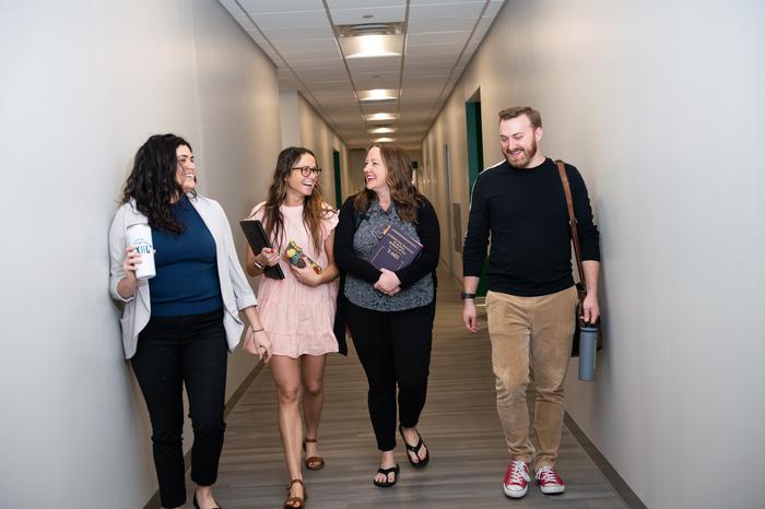 Four students smiling while walking down a hallway in a Jacksonville University building.